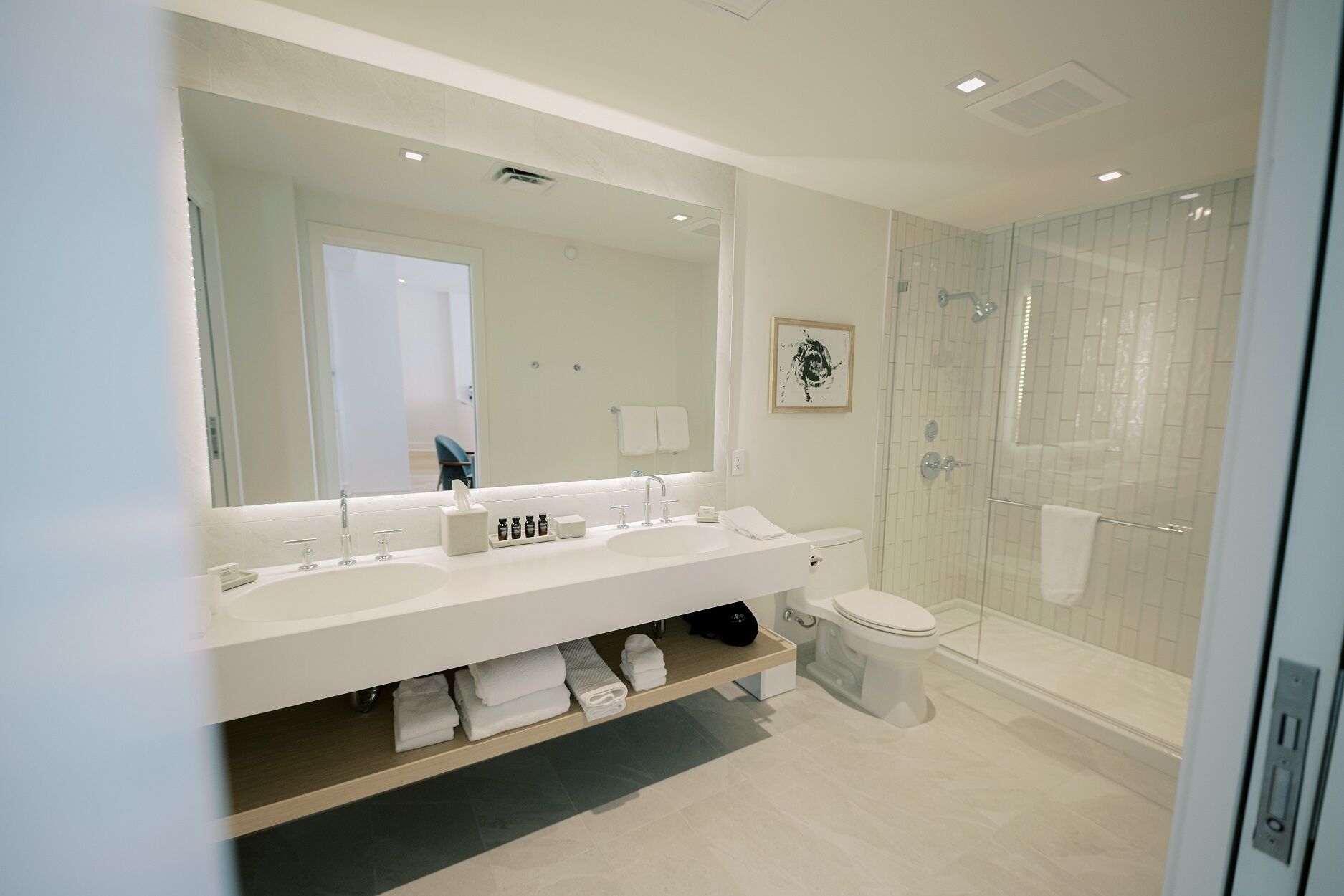 A modern bathroom with a large mirror, two sinks, a toilet, and a glass-enclosed shower.