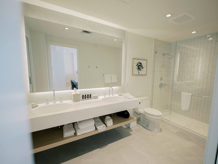 A modern bathroom with a large mirror, two sinks, a toilet, and a glass-enclosed shower.