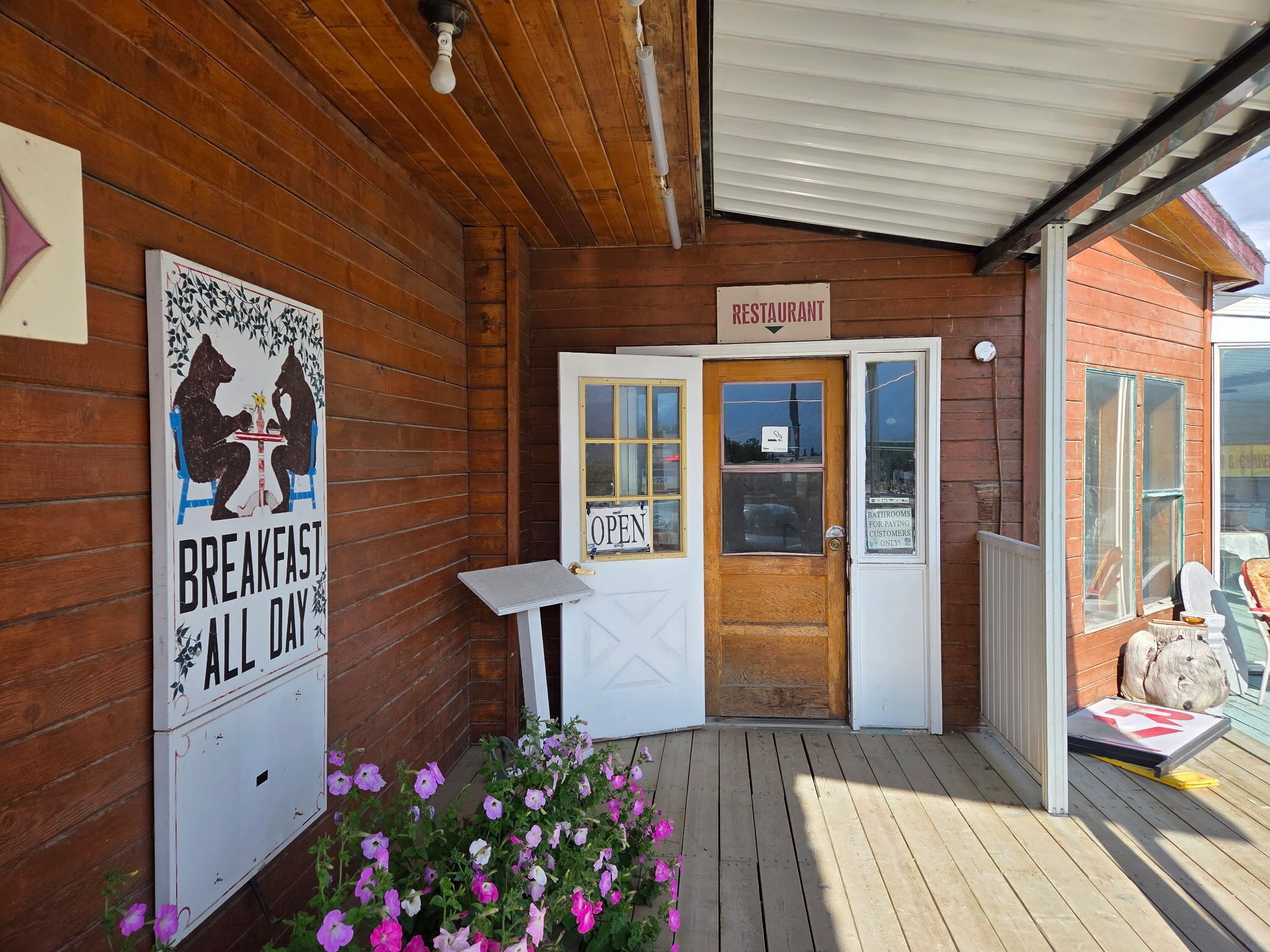 Un bâtiment en bois avec une enseigne indiquant qu’il s’agit d’un restaurant, une porte avec une pancarte « OUVERT » et une autre indiquant que le petit-déjeuner est servi toute la journée.