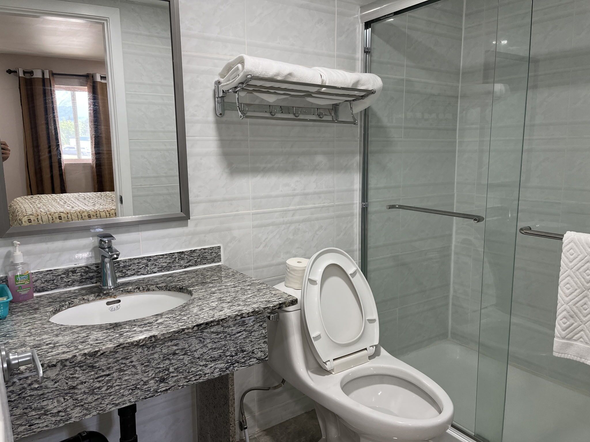 Ein Badezimmer mit Marmorwaschtisch, Toilette, Duschkabine aus Glas und Handtuchhalter.