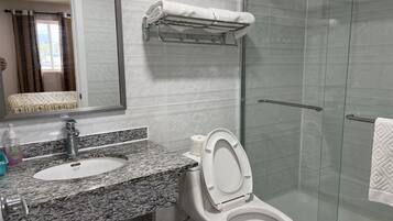 Ein Badezimmer mit Marmorwaschtisch, Toilette, Duschkabine aus Glas und Handtuchhalter.