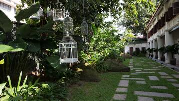 A garden pathway with white birdcages hanging from trees, surrounded by lush greenery and a stone-tiled walkway.