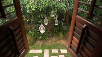 Un sendero en un jardín que conduce a una puerta de madera, rodeado de abundante vegetación y jaulas de pájaros colgantes.