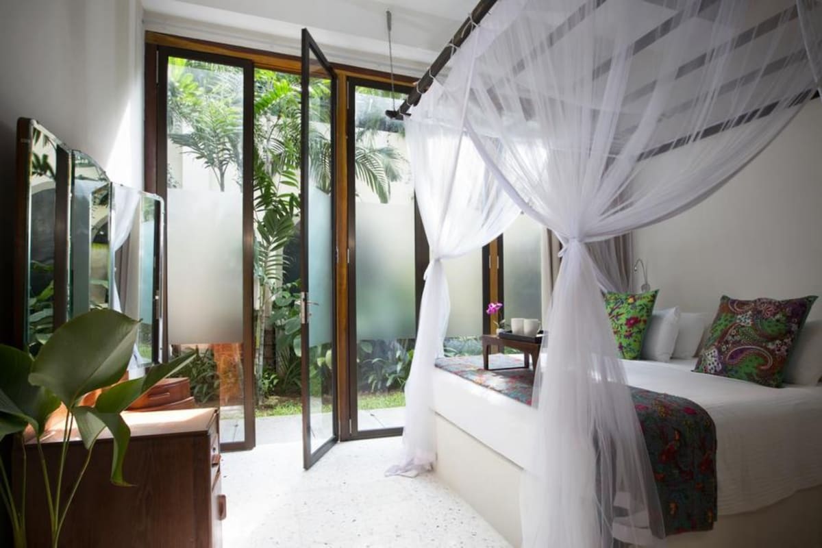 Un dormitorio con cama con dosel, ventanas amplias y vistas a zonas verdes.