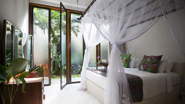 Une chambre avec un lit, une fenêtre donnant sur un espace verdoyant et une porte-fenêtre coulissante qui mène à un espace extérieur.