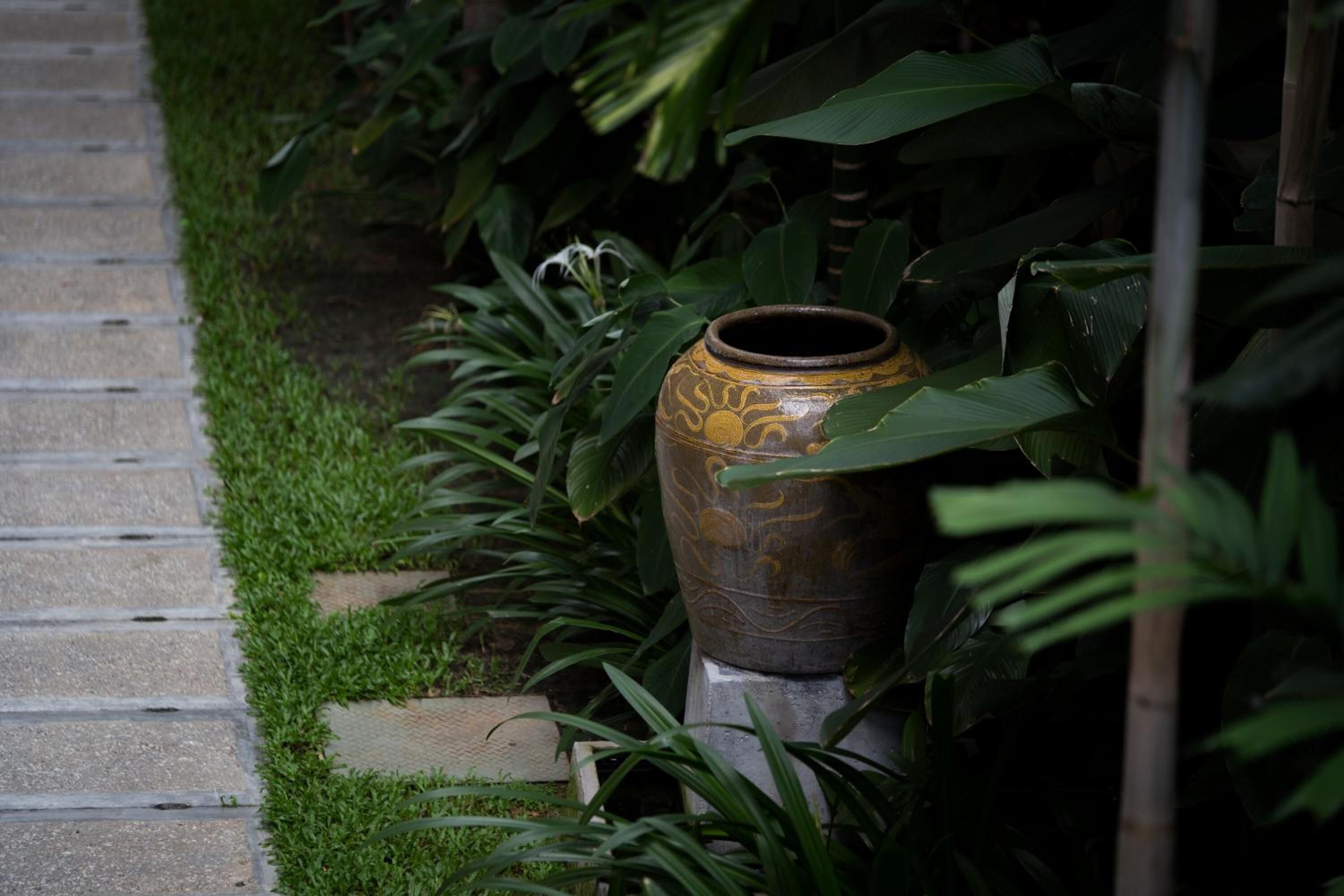 A pathway leading to a large, ornate urn surrounded by lush greenery.