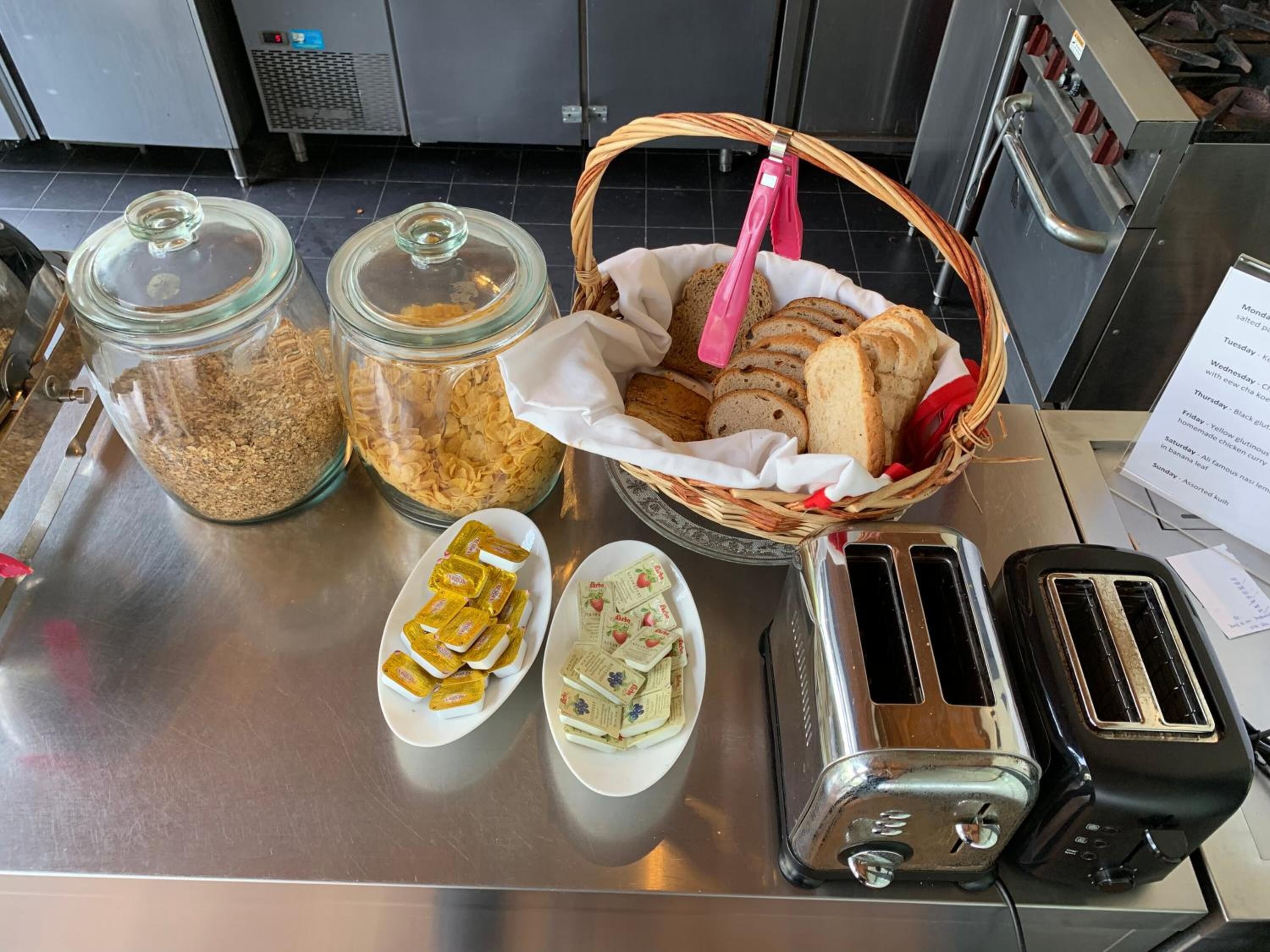 A breakfast buffet with granola, cereal, bread, butter, and jam.