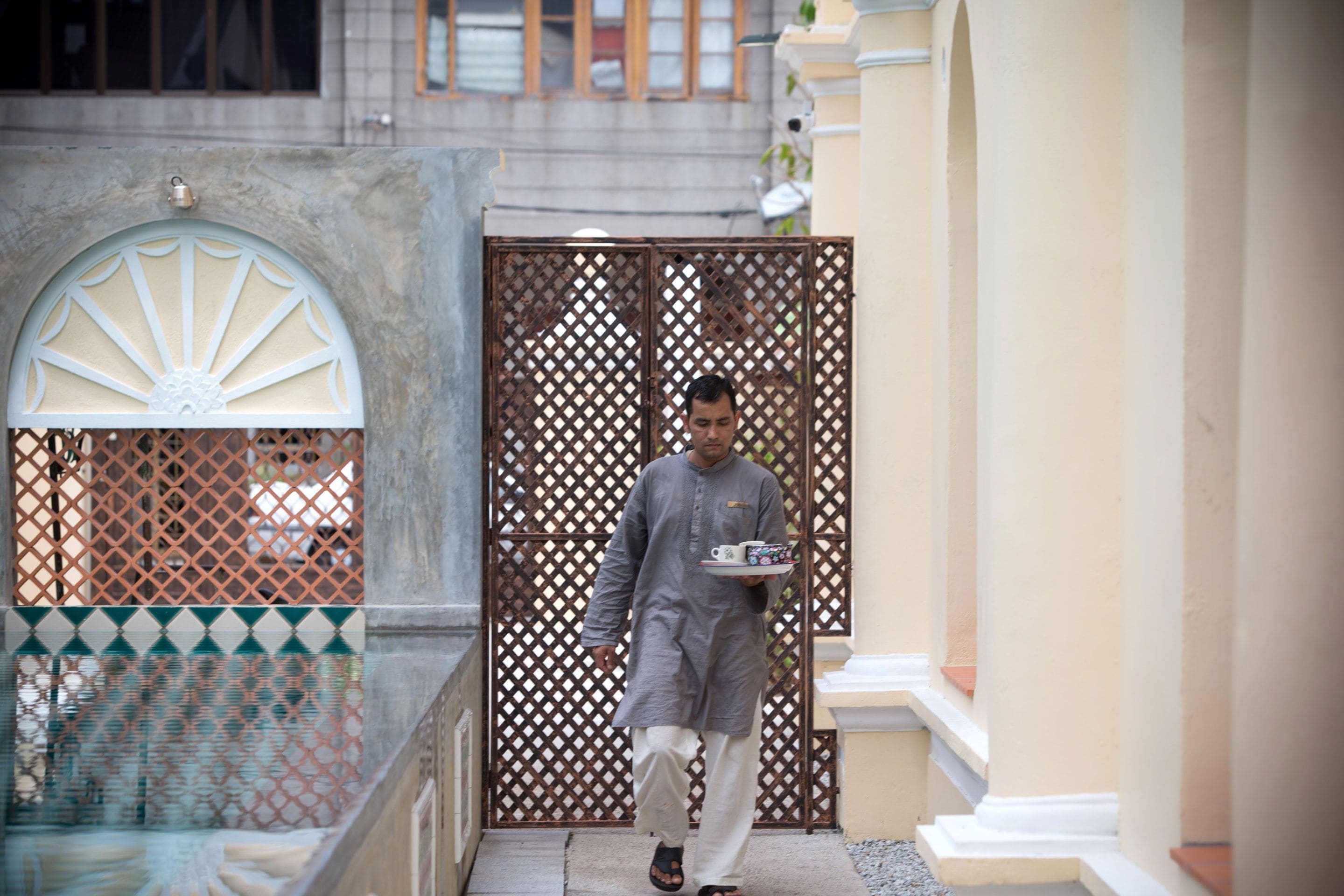 A man in traditional attire walking through a corridor with a tray of items.