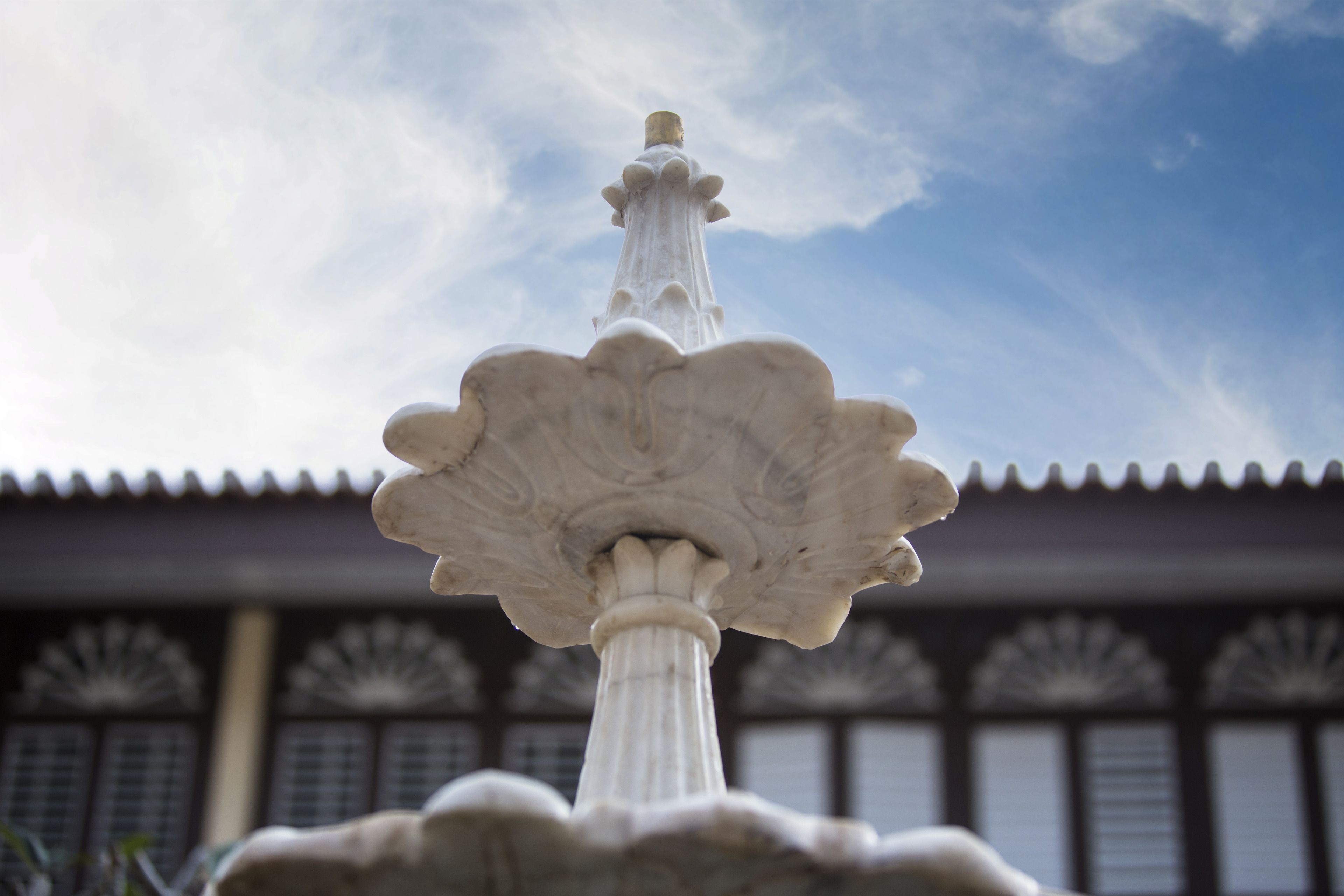 Una fuente de piedra blanca con diseño escalonado, ubicada frente a un edificio con elementos arquitectónicos tradicionales.
