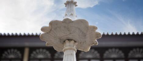 Una fuente de piedra blanca con diseño escalonado, ubicada frente a un edificio con elementos arquitectónicos tradicionales.