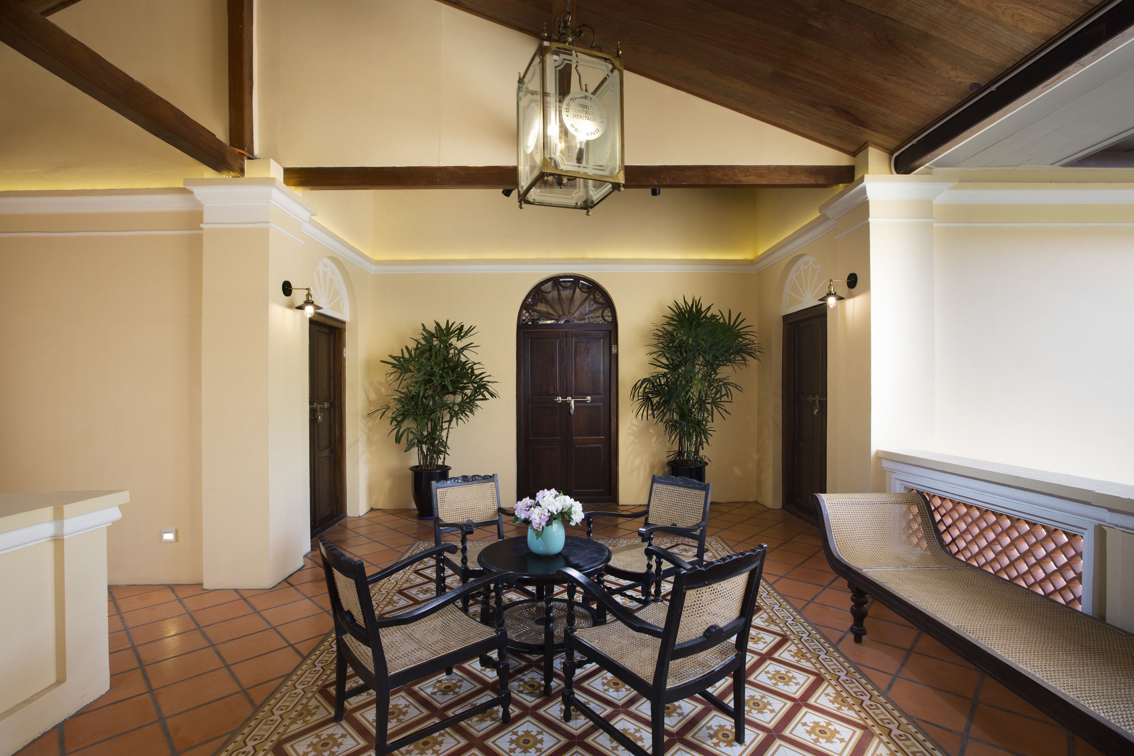 A dining area with a round table, four chairs, a vase with flowers, and two potted plants.