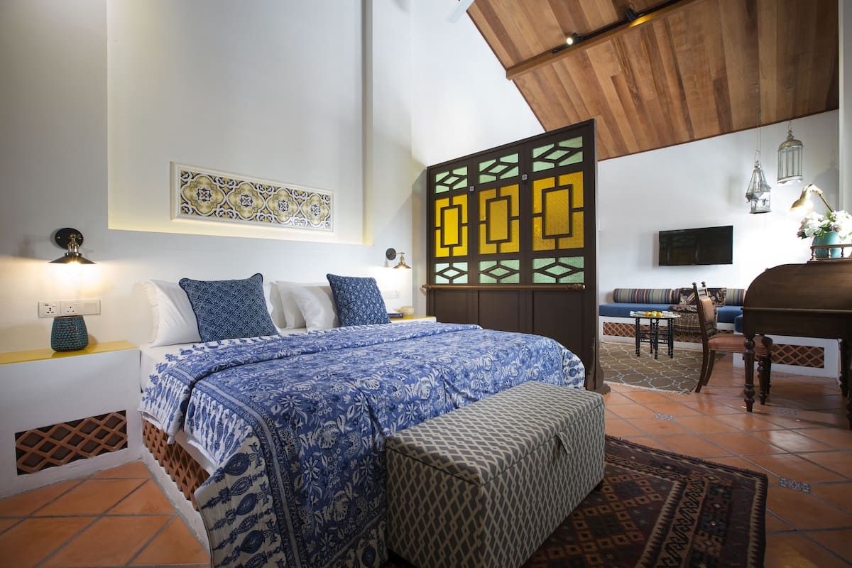 A bedroom with a bed, a bench, a sofa, and a dining area.
