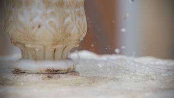 Primer plano de un objeto blanco y ornamentado con superficie texturizada, posiblemente un mueble o un adorno, sobre una superficie con diseño texturizado.