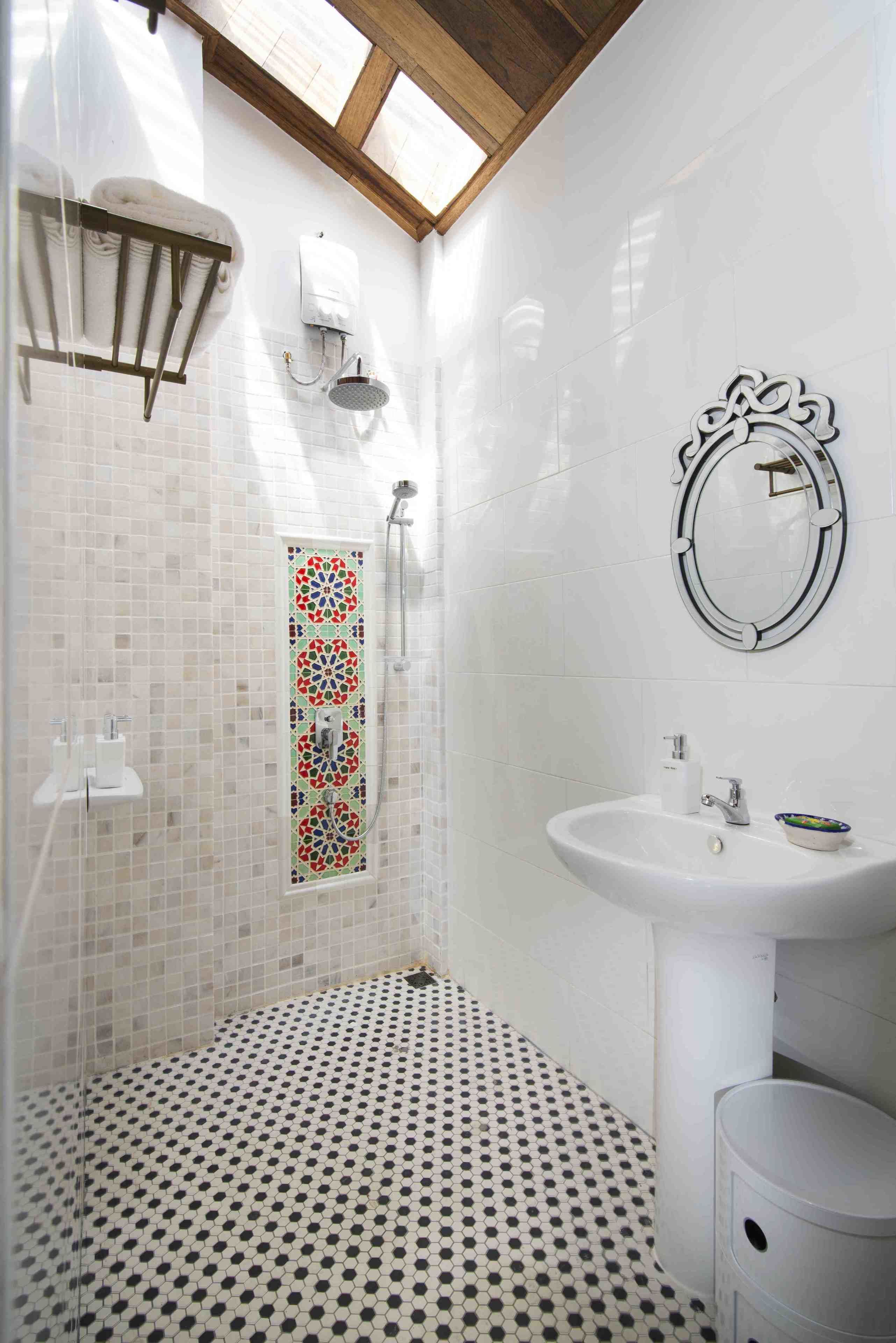 A bathroom with a shower, a sink, a mirror, and a patterned floor.