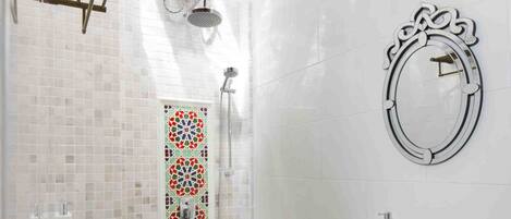 A bathroom with a shower, a sink, a mirror, and a patterned floor.
