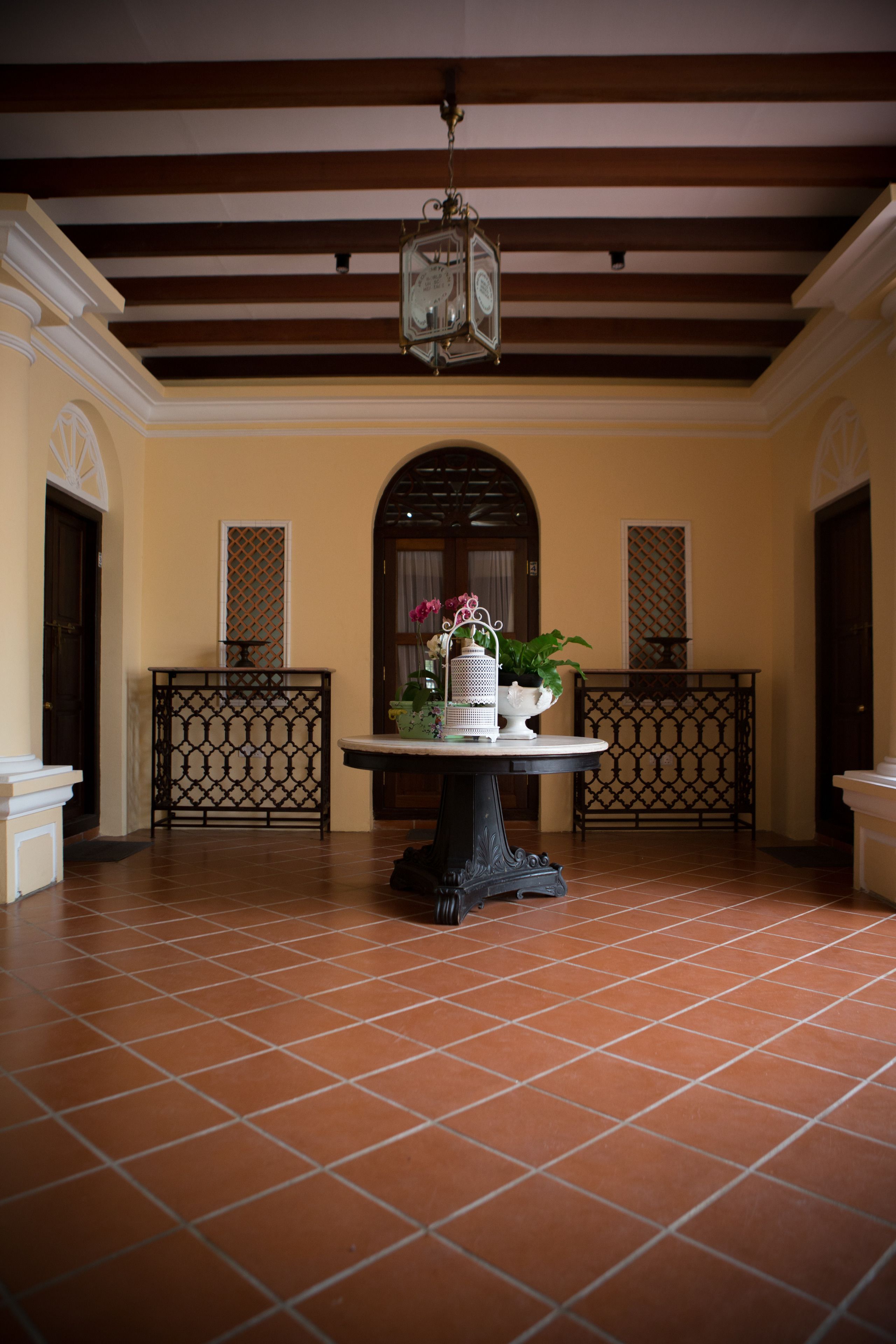 A lobby with a tiled floor, a central table with a potted plant, and a hanging lantern.