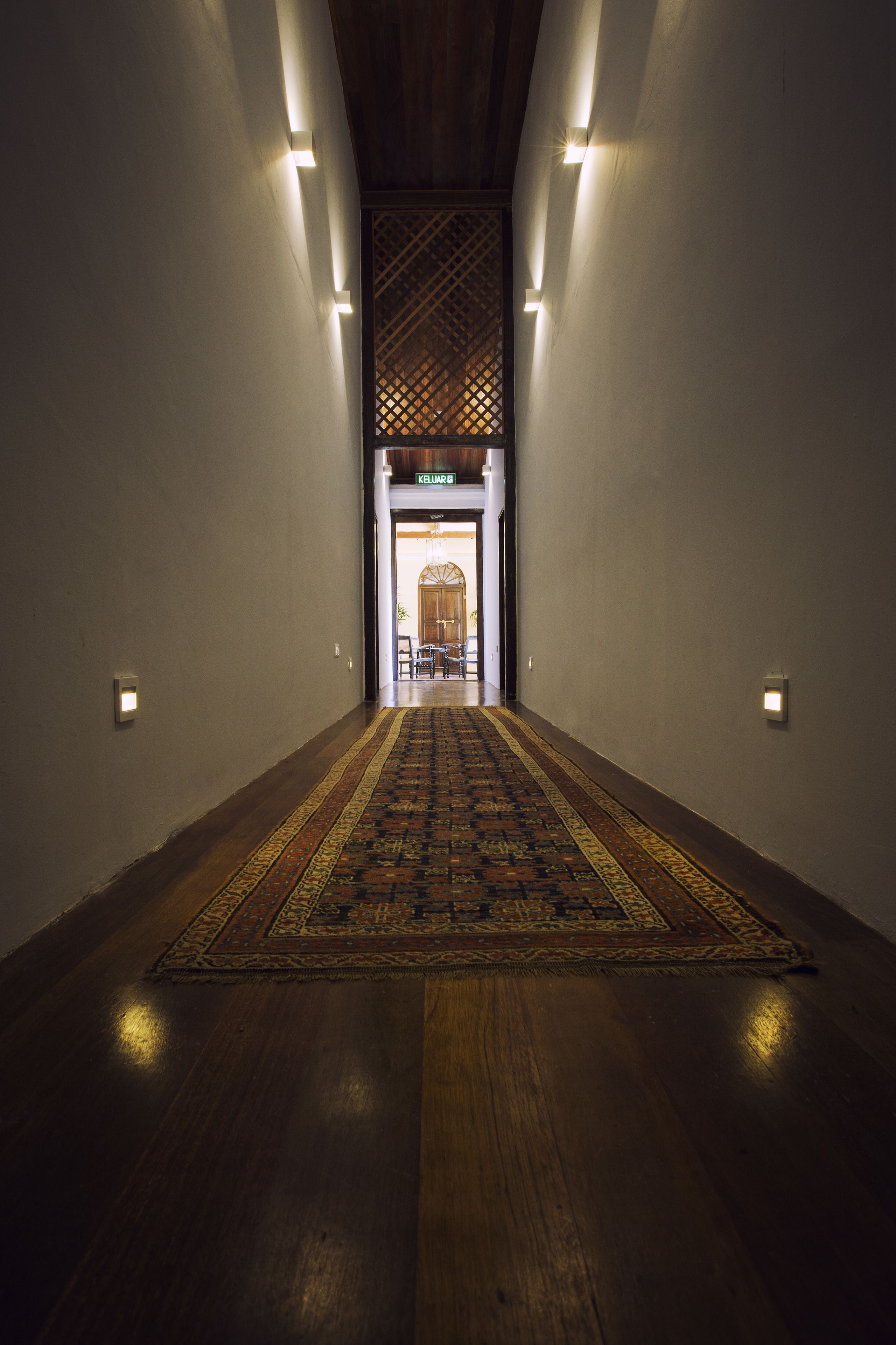 A hallway with a patterned carpet, wooden flooring, and wall-mounted lights.
