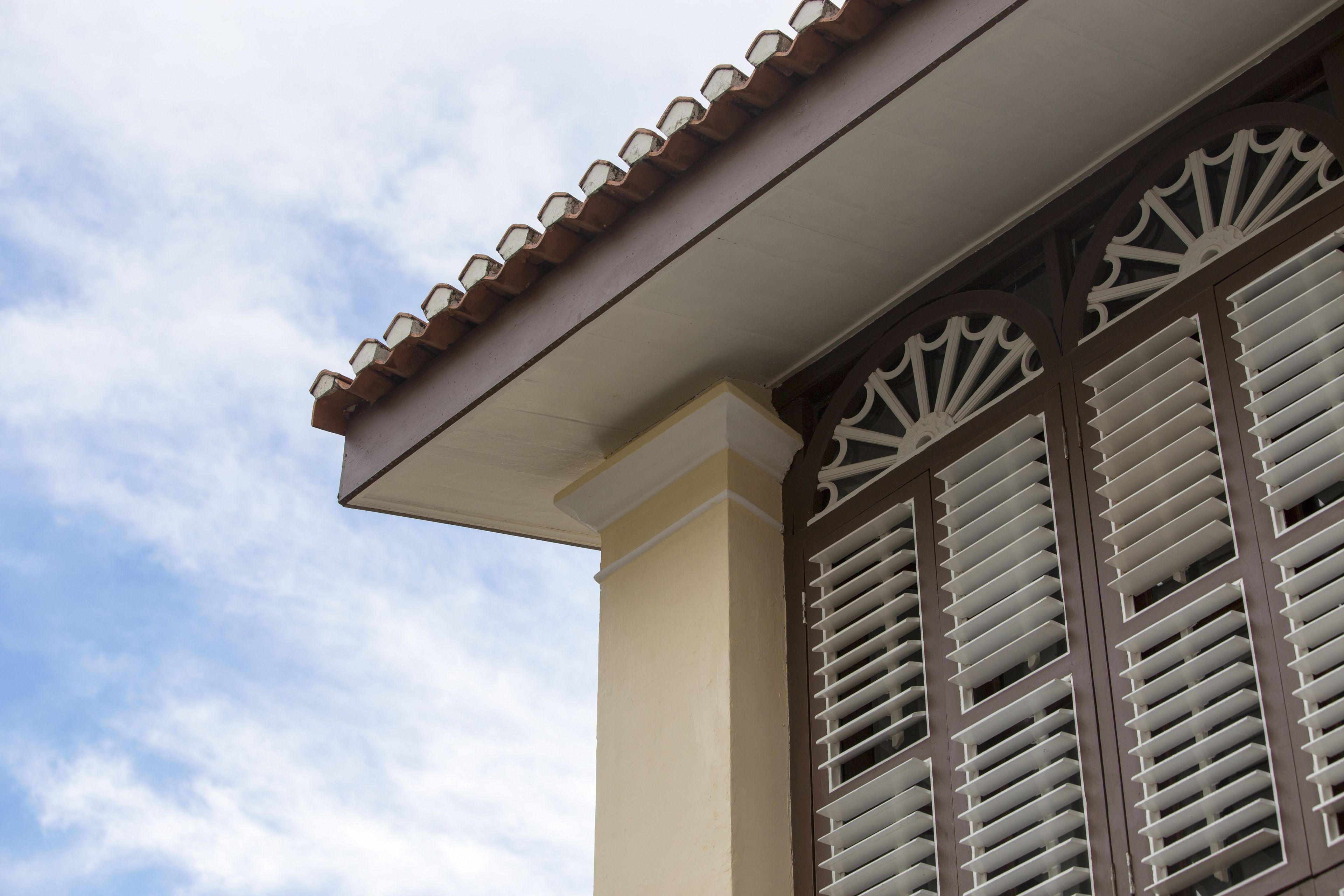 A building with a tiled roof, a beige facade, and a window with horizontal blinds.