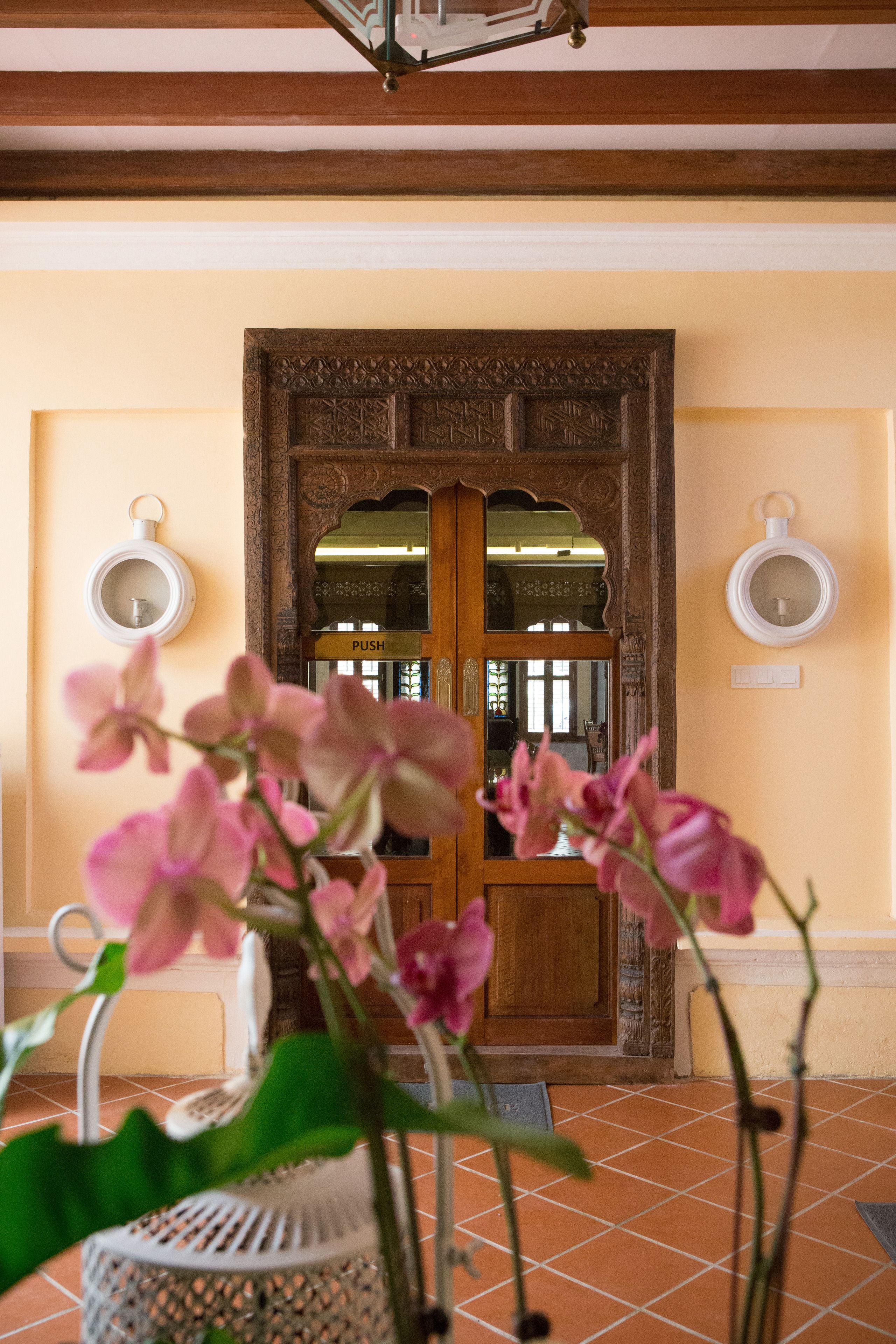 Une porte en bois avec un miroir et une indication « pousser », un mur blanc et, au premier plan, un pot d’orchidée.