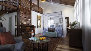 A spacious room with a high ceiling, a wooden staircase, a bed with a canopy, a desk with a chair, and a small table with fruits. - Jawi Peranakan Mansion (George Town)