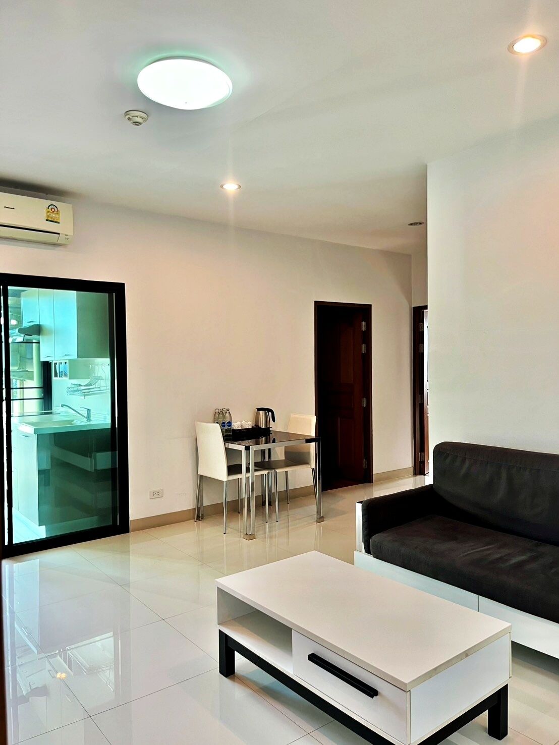 Una sala de estar moderna con una mesa de centro blanca, un sofá oscuro y un comedor con una mesa y sillas.