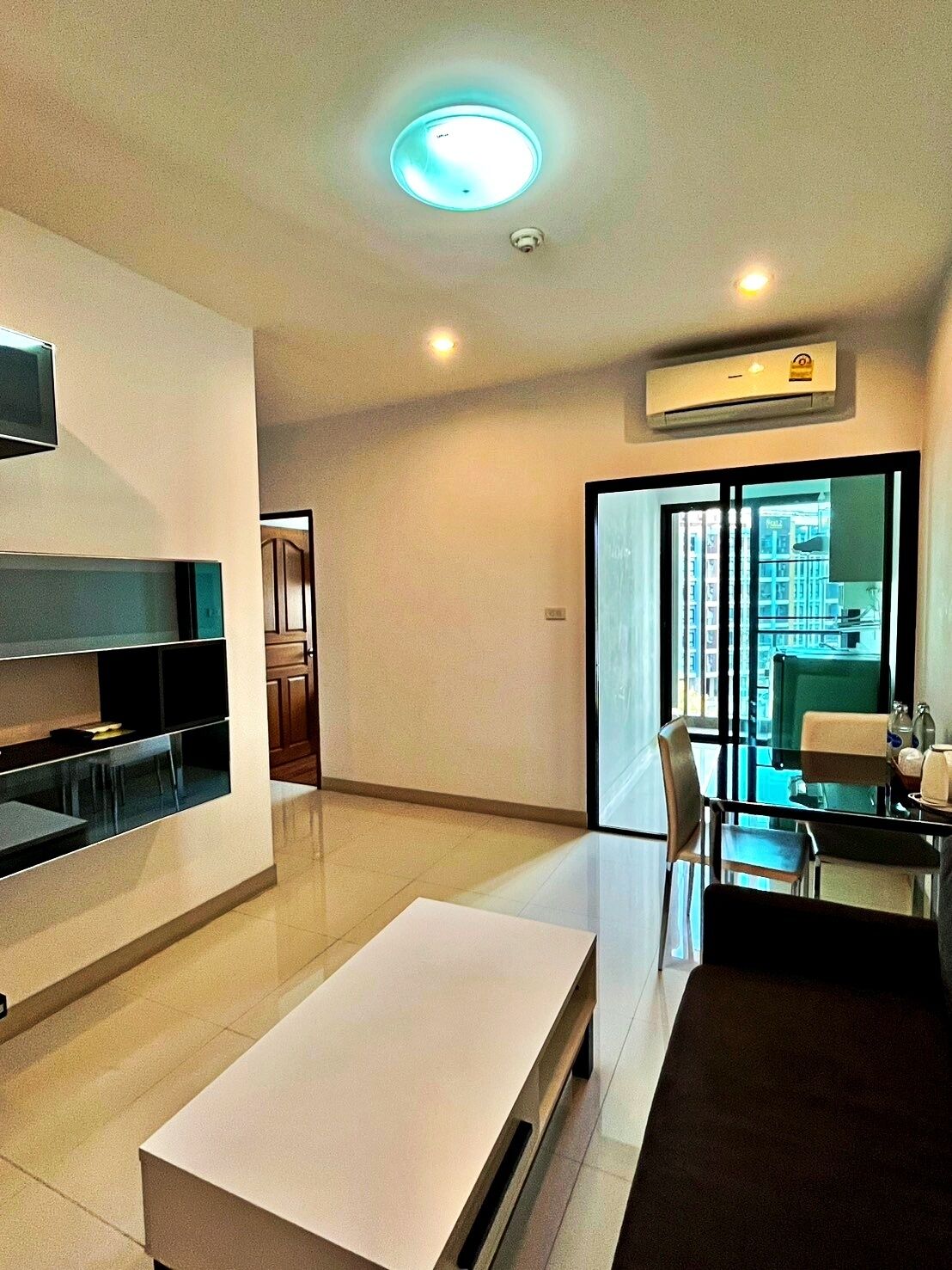A modern living room with a flat-screen TV, a white coffee table, and a dining area with a glass table and chairs.