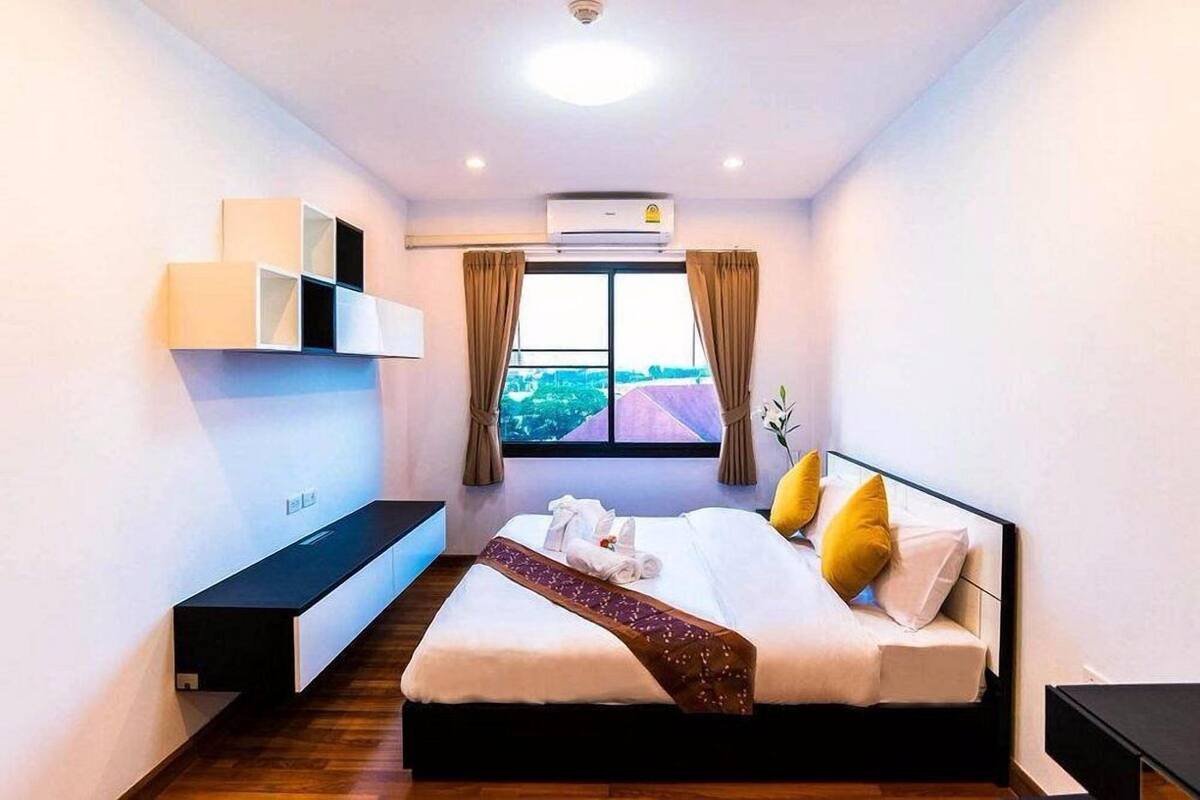 Habitación de hotel con cama, estante empotrado, unidad de aire acondicionado y ventana con cortinas.