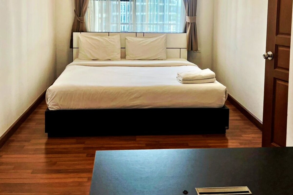 Une petite chambre bien éclairée, avec un lit, des rideaux et un plancher en bois.