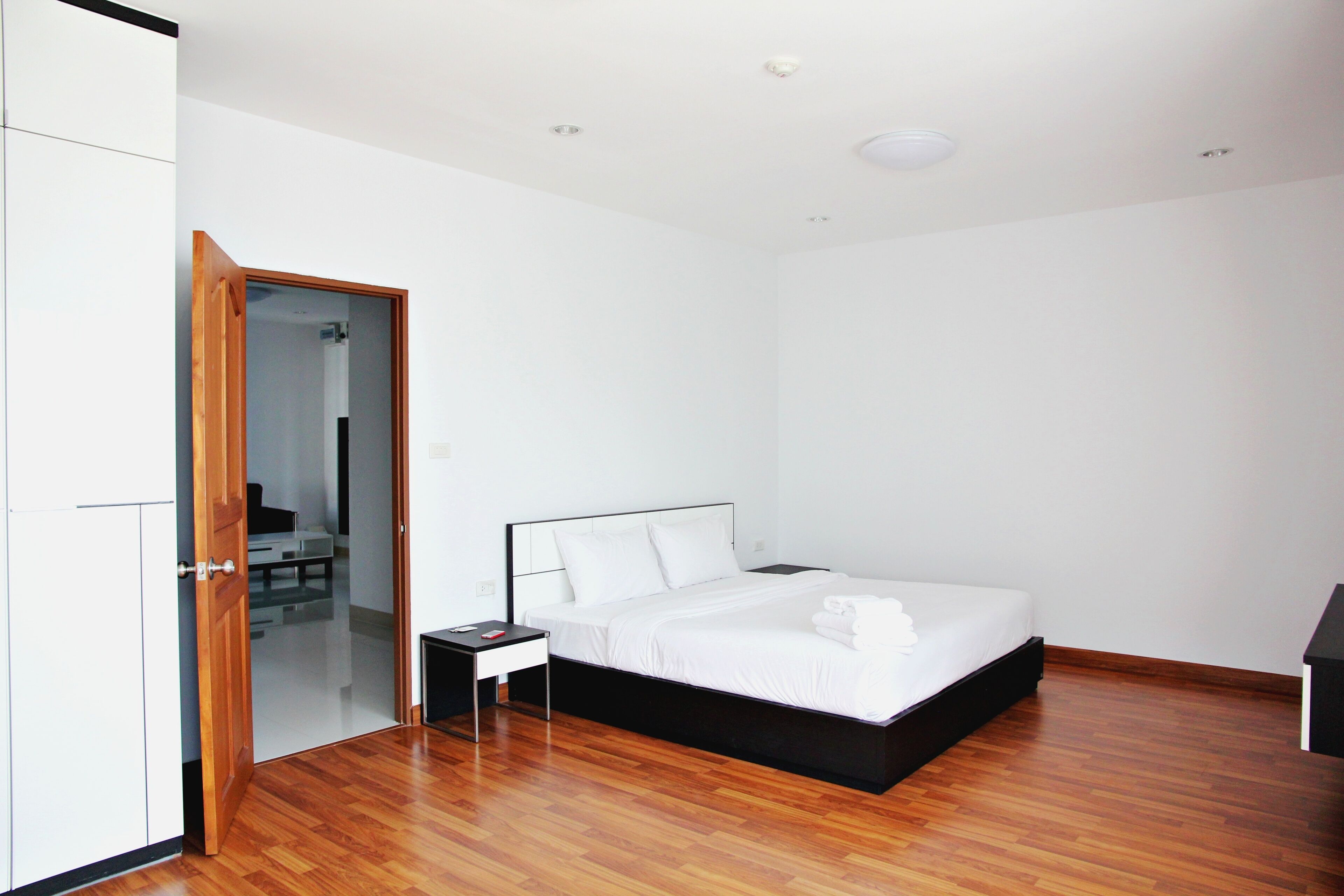 A modern bedroom with a wooden floor, a bed with white linens, a nightstand, and a wooden wardrobe.