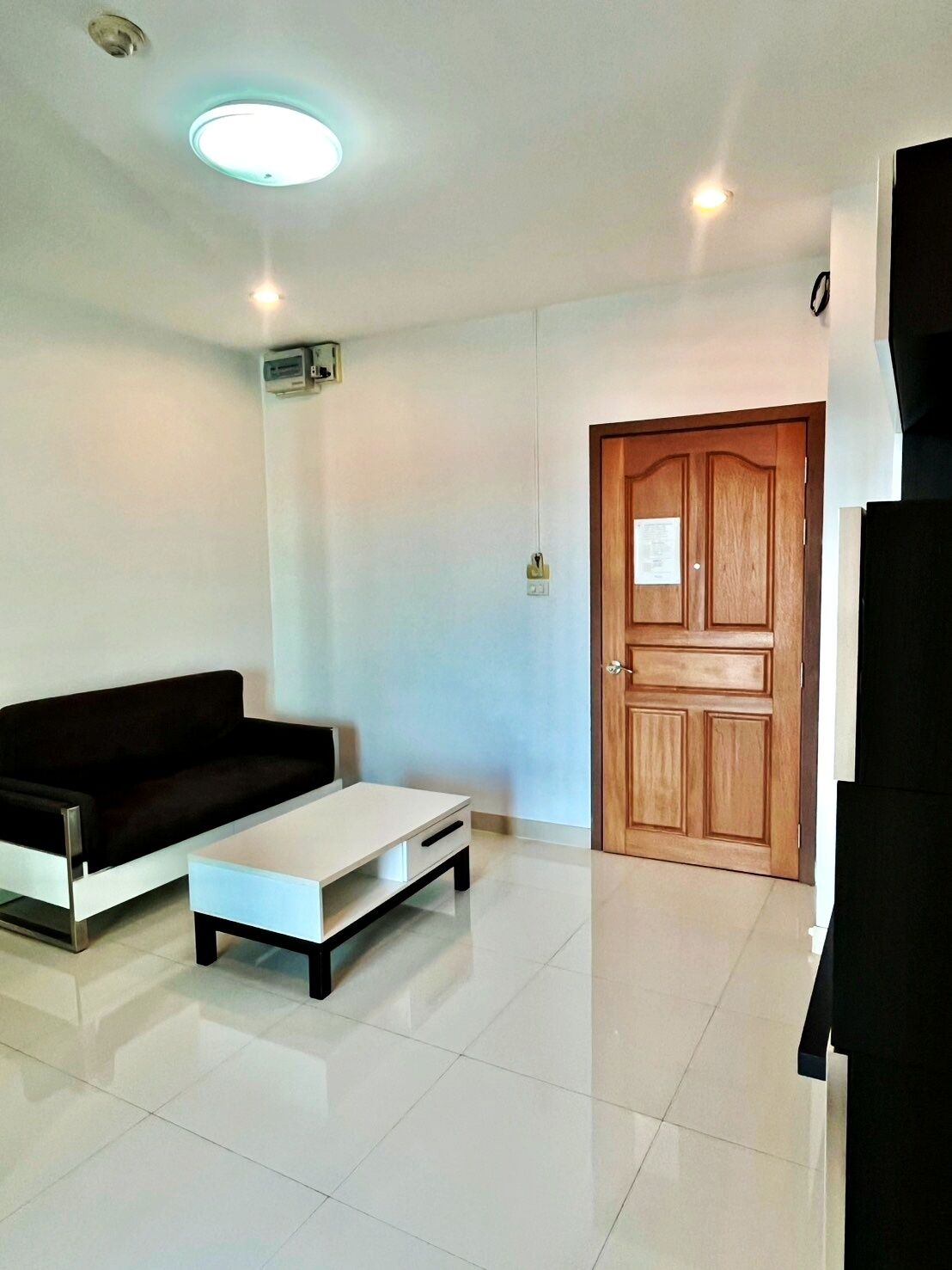 A modern living room with a black sofa, a white coffee table, and a wooden door.