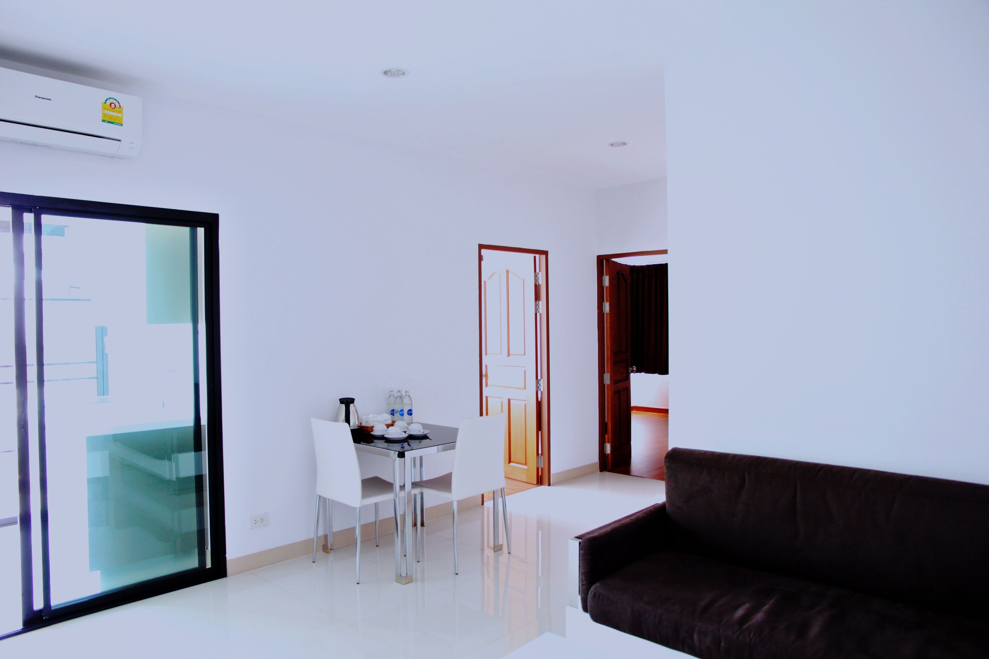 A modern living room with a brown sofa, a dining table with chairs, and a glass door leading to a balcony.