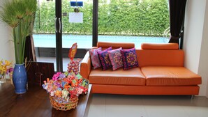 Un salon moderne avec un canapé orange, des coussins décoratifs, un panier en osier rempli de jouets et un vase bleu contenant des plantes vertes.