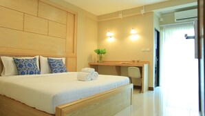 Une chambre d’hôtel avec un grand lit, un bureau et une chaise. Il y a deux lampes fixées au mur et une plante sur le bureau.