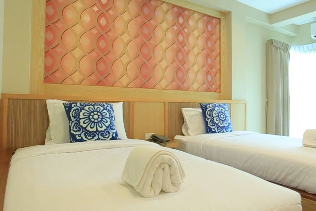 A hotel room with two beds, a decorative headboard, a telephone, and an air conditioning unit.