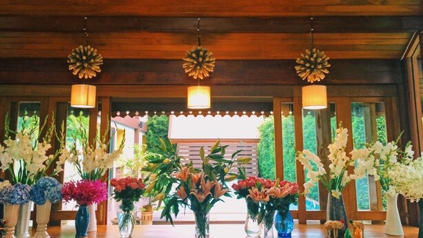 Un intérieur en bois avec un comptoir d’accueil agrémenté de divers arrangements floraux et de luminaires décoratifs suspendus.