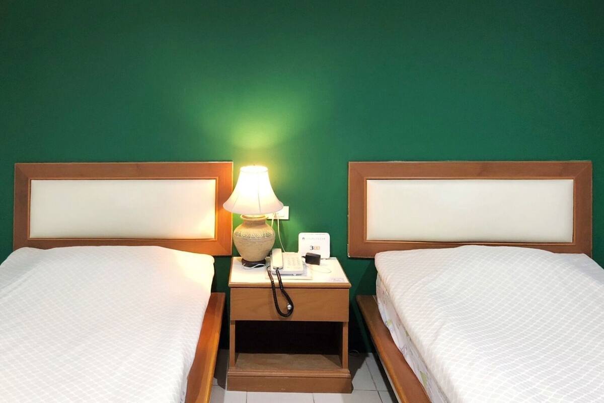 Ein Hotelzimmer mit zwei Betten, einer Nachttischlampe, einem Telefon und einem Nachttisch.