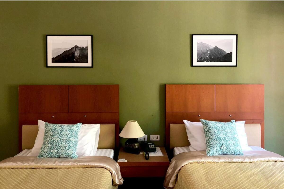 Ein Hotelzimmer mit zwei Betten, jeweils mit einem Holz-Kopfteil, einem Nachttisch mit Lampe und einem gerahmten Bild an der Wand.