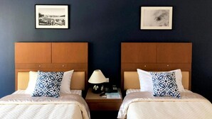 Een hotelkamer met twee bedden, elk met hoofdeinde, een nachtkastje met lamp en ingelijste foto's aan de muur.