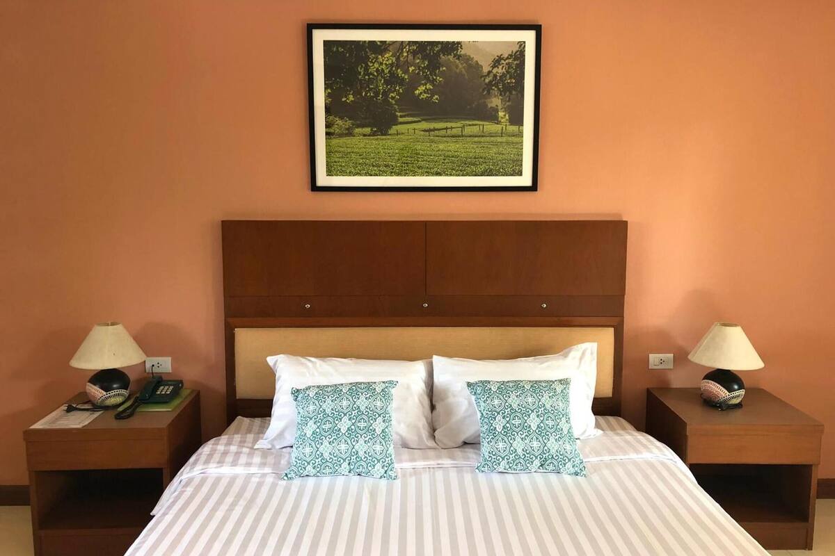 Ein Hotelzimmer mit einem großen Bett, zwei Nachttischen, einem gerahmten Bild eines Feldes und einem hölzernen Kopfteil.
