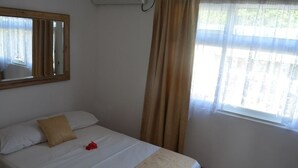 A bedroom with a bed, a mirror, and a window with curtains.