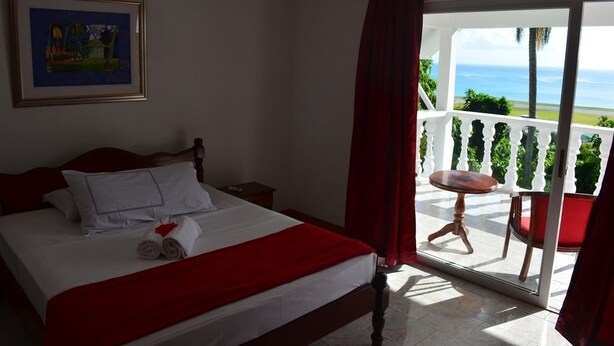 A hotel room with a bed, a painting on the wall, and a balcony with a view of the ocean.