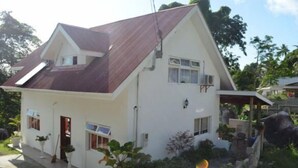 A two-story house with a sloped roof, a front porch, and a small garden area.