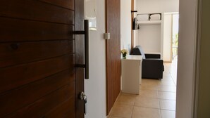 A wooden door leading to a room with a white wall, a small white table, and a black sofa. - King's Holiday Apartments (Paphos)
