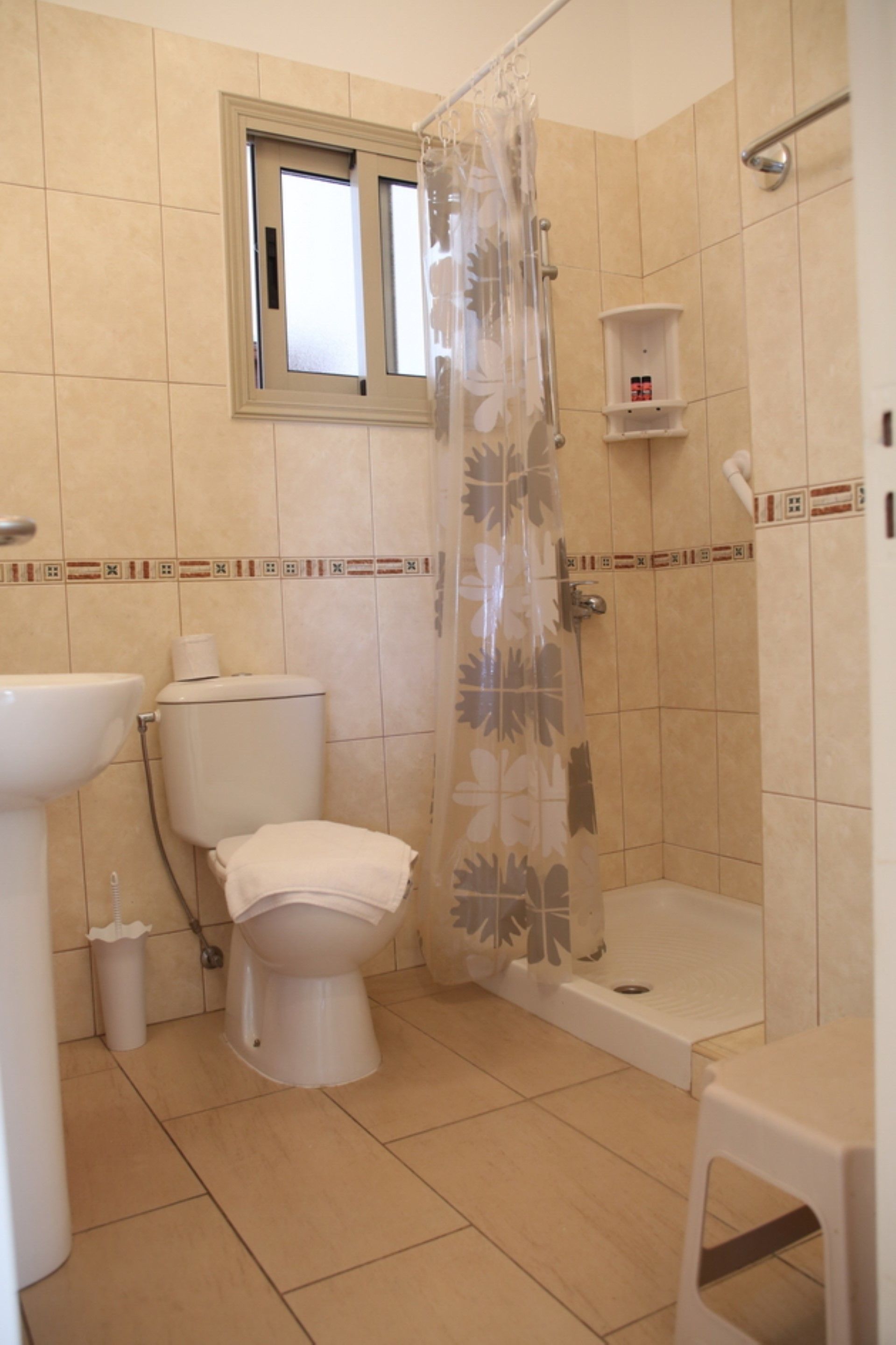 A bathroom with a toilet, sink, shower, and a window.