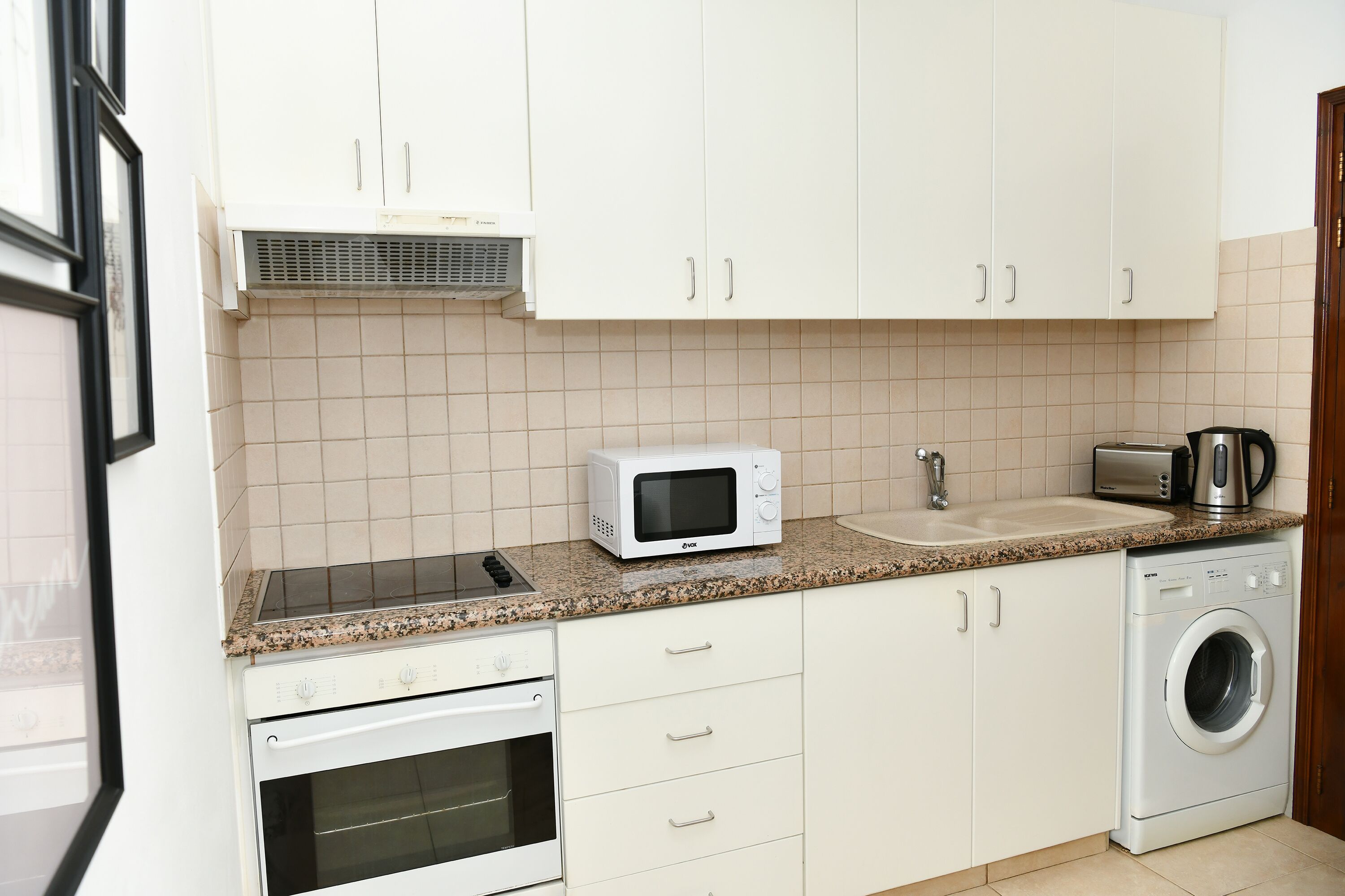 A kitchen with white cabinets, a microwave, a toaster, a sink, and a washing machine.
