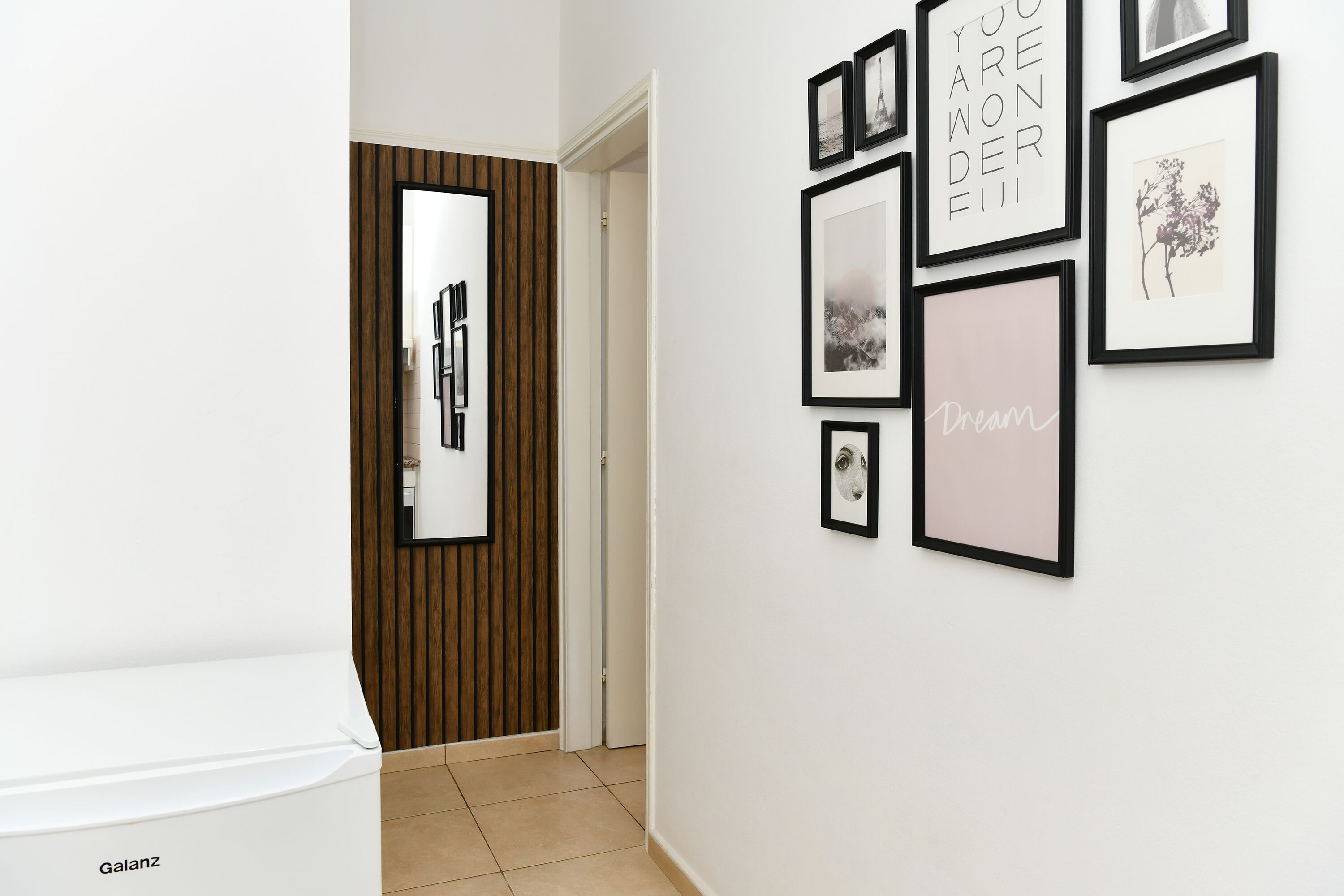 A hallway with framed pictures on the wall, a door with a mirror, and a white appliance labeled 'Galanz' on the left.