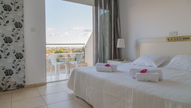 A hotel room with a balcony, a bed with white linens, and a view of the outdoors. - King's Holiday Apartments (Paphos)