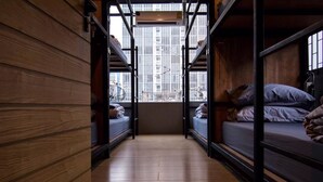 A narrow corridor with bunk beds on either side, wooden walls, and a window with a cityscape view. - Nap@Pan Hostel (Bangkok)