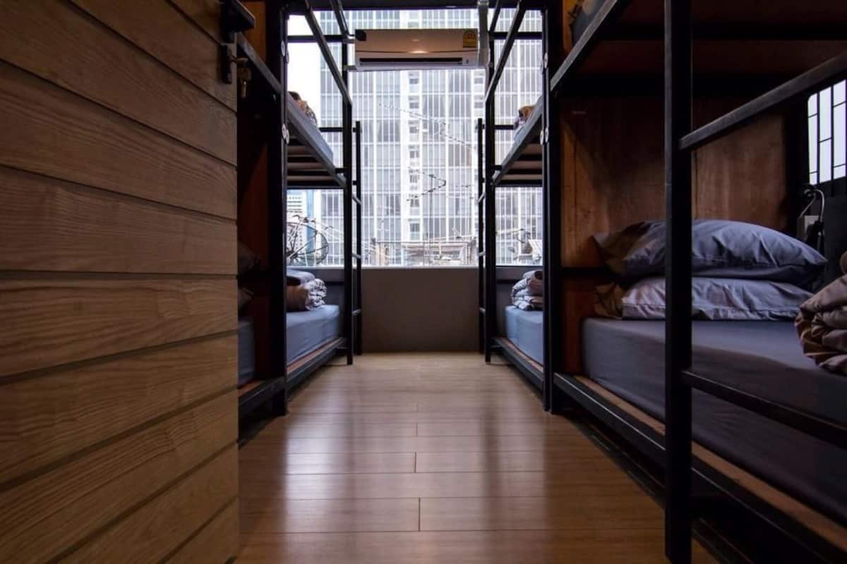 A narrow corridor with bunk beds on either side, wooden walls, and a window with a cityscape view.