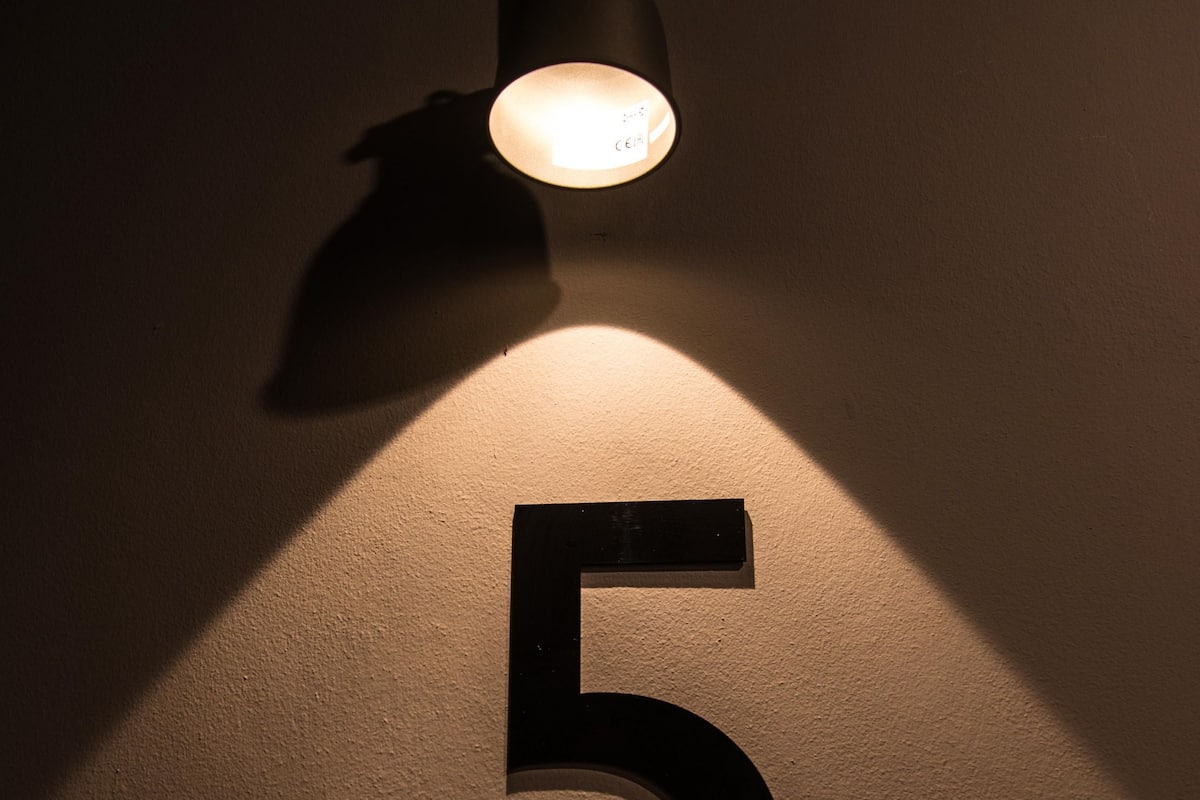 A wall-mounted number "5" illuminated by a spotlight.